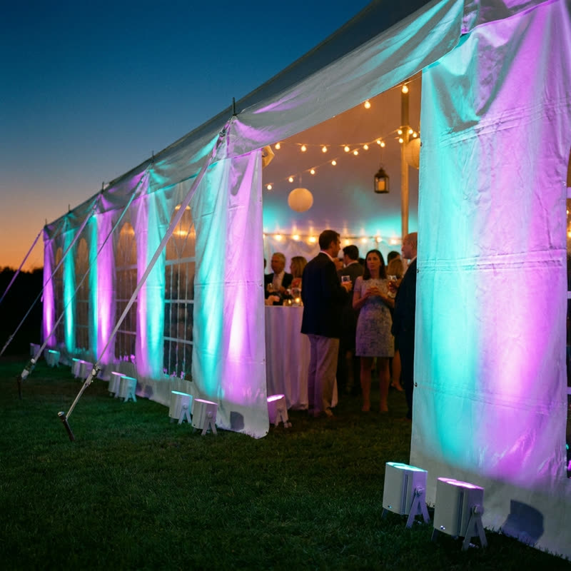 LED up-lights washing an event tent in purple and teal at dusk